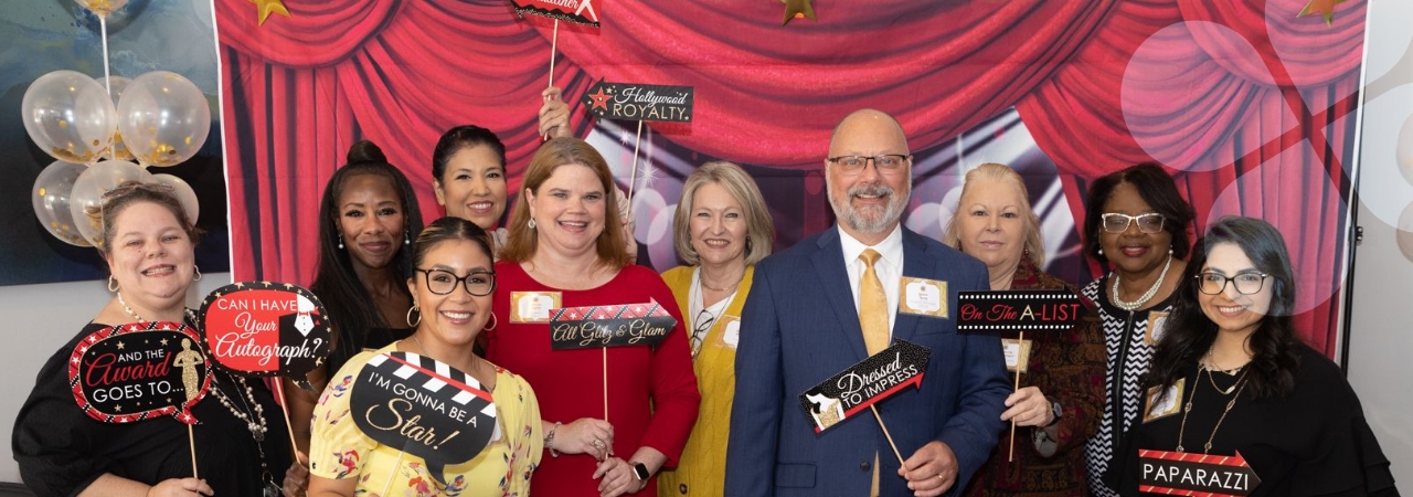 Harris Center staff in a decorated space, smiling for a group photo and holding career-related signs
